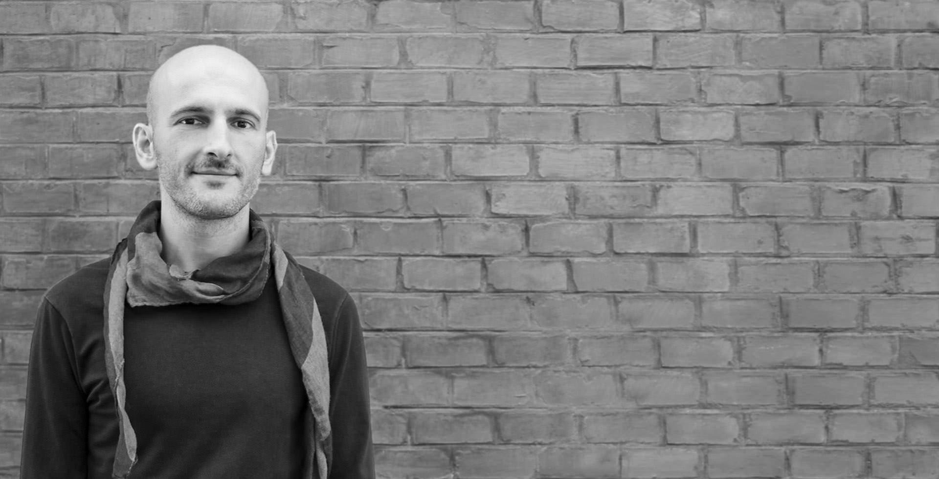 Gabriele Web Designer smiles leaning against an exposed stone wall